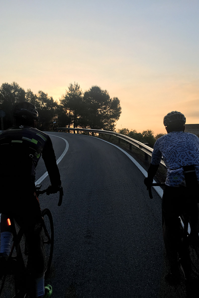 dos ciclistas en ruta con bici de carretera con la salida del sol de fondo