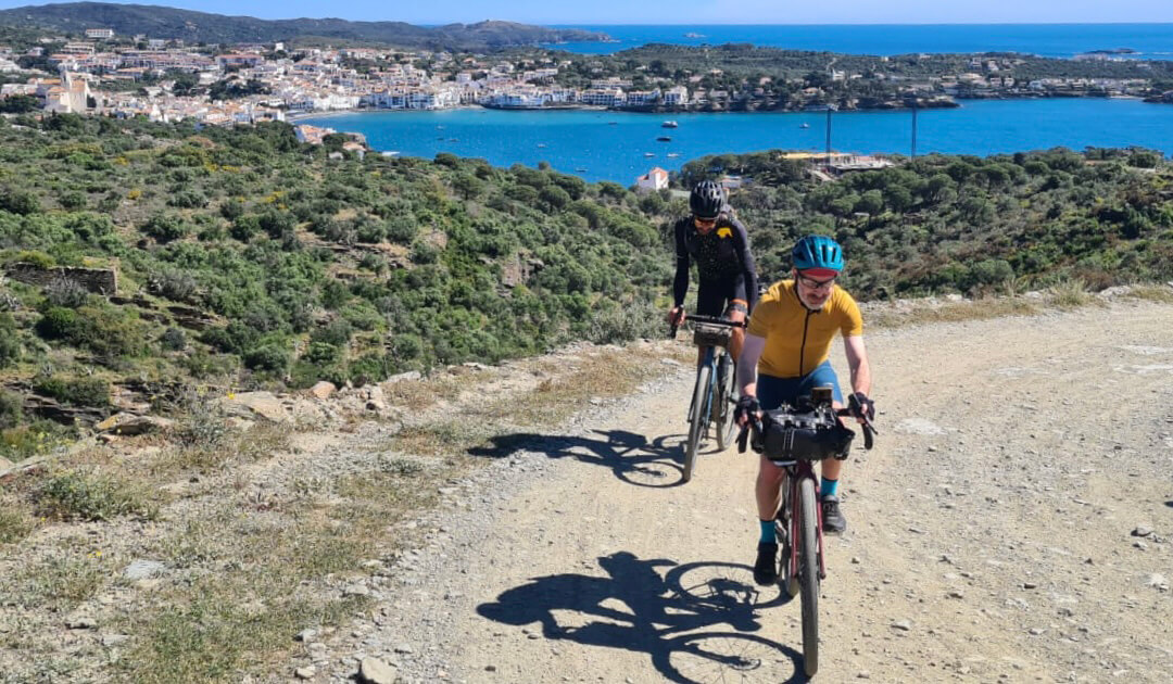 Dos ciclistas en bici de gravel con Cadaqués y el Mar Mediterráneo de fondo